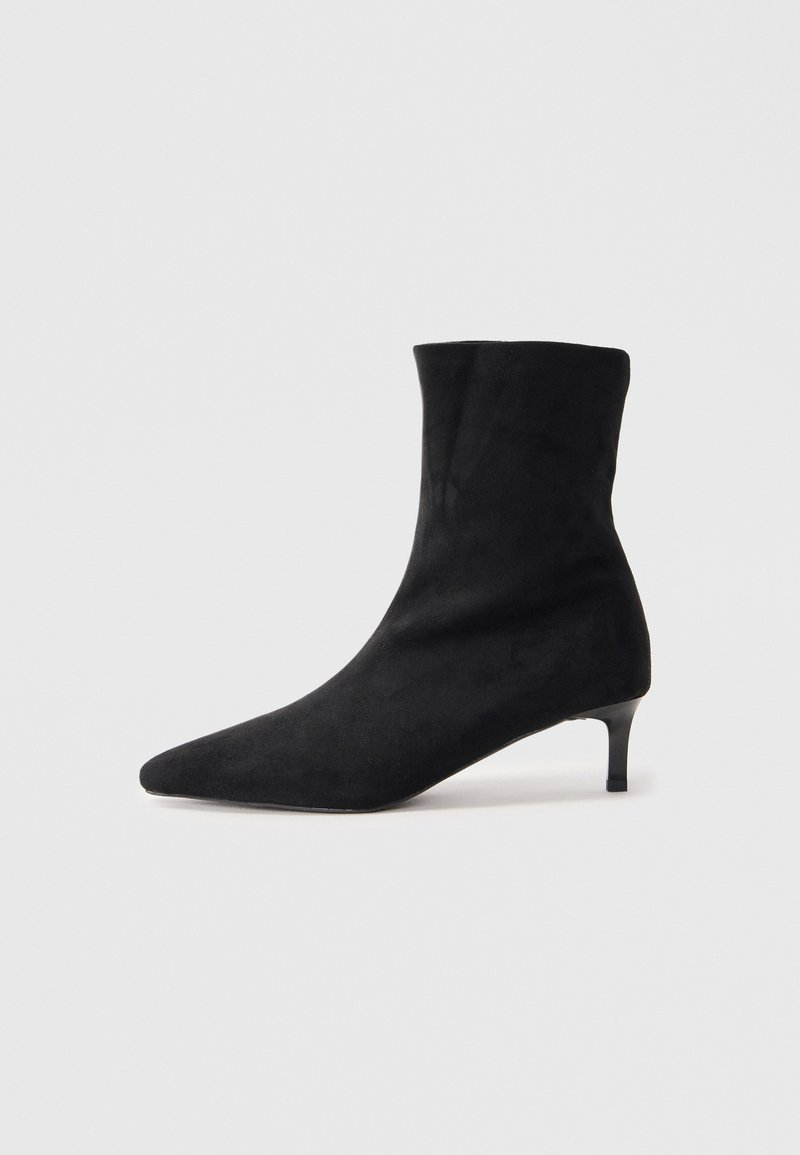 Stivale alla caviglia in suede nero con punta appuntita e tacco sottile e leggermente curvato. Texture liscia e design minimalista.