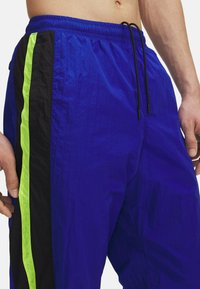Blauwe lichtgewicht shorts met een zwart zijpaneel en neon groene accentstrip. Voorzien van een elastische tailleband en een trekkoord voor aanpassing.