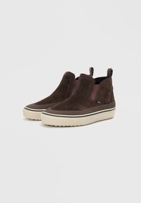 Brune semskede slip-on sko med elastiske sidepaneler og hvide gummisåler. Har sort og hvid stribet detalje på sålen.