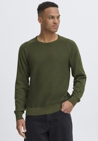 Suéter de punto verde oliva con mangas largas, puños acanalados y cuello redondo. Presenta una tela texturizada y un ajuste relajado.