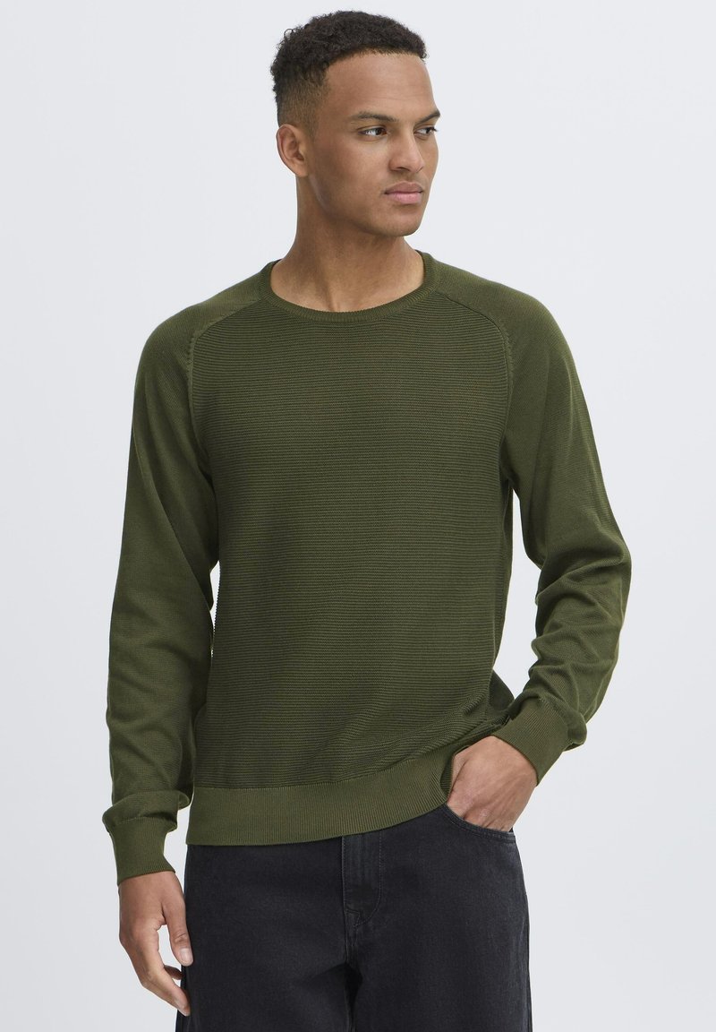 Suéter de punto verde oliva con mangas largas, puños acanalados y cuello redondo. Presenta una tela texturizada y un ajuste relajado.