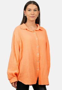 Camicia arancione con bottoni, realizzata in un tessuto leggero e texture, dalla vestibilità rilassata, colletto e maniche lunghe con polsini. Presenta bottoni bianchi lungo la parte anteriore.