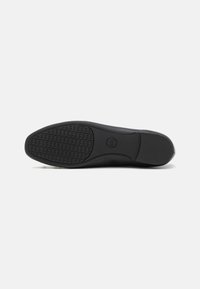 Suela de zapato de goma negra con un patrón texturizado de agarre y bordes redondeados, con un logotipo impreso en el centro.