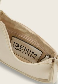 Witte neplederen handtas met een gladde textuur, ritssluiting en beige stoffen voering met een logotag aan de binnenzijde.