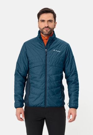 Giacca isolante teal con chiusura a zip e motivo trapuntato. Presenta tasche laterali e un colletto alto. Indossata sopra un top arancione.