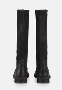 Bottes noires en cuir jusqu'au genou avec une finition lisse, des textures duales, des accents de couture, et un talon empilé. La vue arrière met en avant un design élégant.