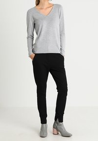 Maglione grigio chiaro a maniche lunghe con scollo a V abbinato a pantaloni jogger neri e stivaletti grigi alla caviglia con tacco a blocco rosa. Tessuto morbido e vestibilità rilassata.