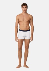 Pantaloni boxer bianchi in cotone con una vita blu navy che presenta il marchio "HACKETT." Il design è semplice e aderente.