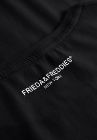 Zwarte t-shirt met een gladde katoenstructuur, voorzien van witte bedrukte tekst "FRIEDA & FREDDIES NEW YORK" nabij de hals.