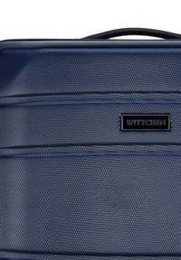 Valigia rigida blu navy con superficie testurizzata, dotata di un prominente etichetta nera del marchio e accenti a scanalature orizzontali.