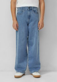 Niebieskie szerokie spodnie jeansowe z wysokim stanem, wyposażone w szlufki na pasek, przednie kieszenie i luźny krój, połączone z białymi trampkami.