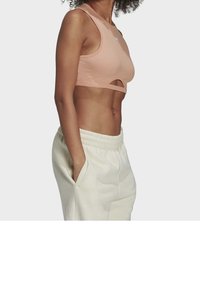 Jasnoróżowy prążkowany crop top z bezrękawnikowym krojem, z wycięciem z przodu. Połączony z luźnymi białymi spodniami dresowymi.