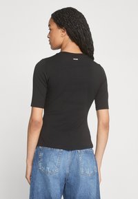 Black short-sleeve fitted t-shirt with a round neckline and logo at the back, paired with light blue loose-fitting denim jeans.