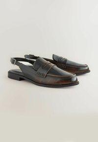 Mocassini slingback in pelle marrone scuro con punta arrotondata, dettagli di cucitura sottili e tacco basso e piatto. Include una cintura regolabile alla caviglia.