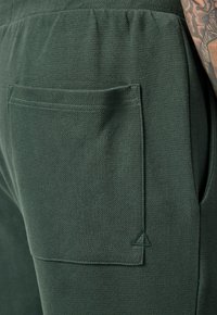 Joggers verdes texturizados con un bolsillo trasero y un logotipo en triángulo cosido en el mismo color. Cintura elástica para mayor comodidad.
