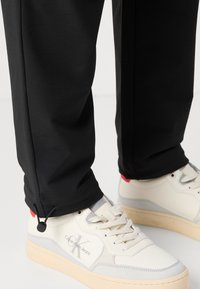 Svarte joggebukser med snøring og mansjett, kombinert med hvite sneakers med grå detaljer. Materialet ser mykt og stretchy ut.