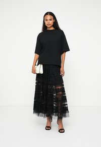 Must värviline oversize t-särk, kombineeritud kihilise musta pitsist pika seeliku ja väikese valge käekotiga. Mudel kannab musti avatud varvastega kingi.