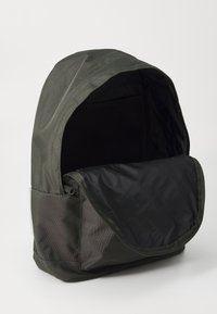 Mochila de tecido verde-escuro com topo aberto, apresentando um forro interior preto e um bolsinho lateral com fecho. Textura suave.