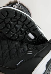 Czarne wodoodporne zimowe buty z pikowanej tkaniny, futrzanym wykończeniem i grubymi gumowymi podeszwami z misternym wzorem bieżnika.