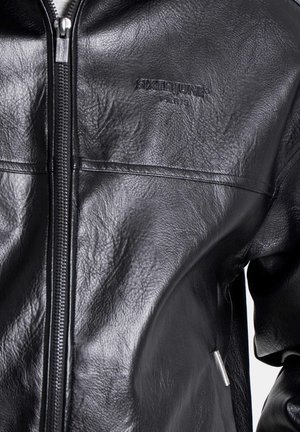 Schwarze Lederjacke mit Reißverschluss, strukturierter Oberfläche und eingeprägtem Logo. Das Design besticht durch schlanke Linien und dezente Hardware-Akzente.