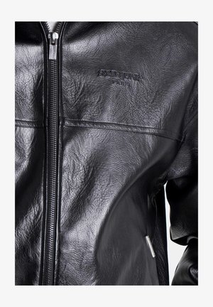 Schwarze Lederjacke mit Reißverschluss, strukturierter Oberfläche und eingeprägtem Logo. Das Design besticht durch schlanke Linien und dezente Hardware-Akzente.