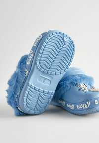 Blaue Clogs mit weichen blauen Kunstfellakzenten, ausgestattet mit einer strukturierten Gummisohle und "Bluey"-Branding in Weiß an der Seite.