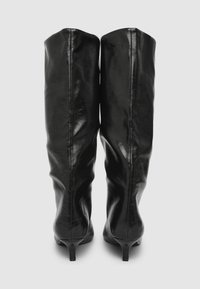 Stivali neri in pelle al ginocchio con finitura lucida, design affusolato e tacco sottile. Presentano una cucitura che corre lungo la parte posteriore.