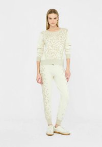 Komplet udobne odjeće u krem boji s dizajnom leopardskog uzorka, rebrastim manžetama i odgovarajućim hlačama s elastičnim pojasom, uparen s bijelim tenisicama i suptilnim naglascima.