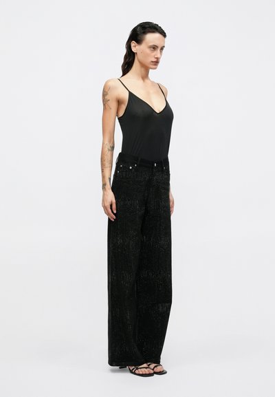 Top nero senza maniche con spalline sottili e scollatura a V abbinato a pantaloni neri a gamba larga con un motivo testurizzato e scintillante.