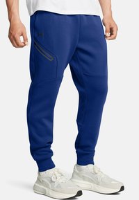 Blauwe joggingsbroek van zacht materiaal, met een ritszak aan de zijkant, taps toelopende benen en geribbelde boorden. Geaccentueerd met een zwart logo.