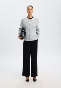 Gray knitted cardigan with round buttons, paired with black wide-leg trousers and pointed black heels. The model holds a black handbag.