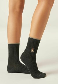 Mørkegrå ribbede ankelstrømper med en guldaccentueret manchet og broderet teddy-bear design nær anklen. Blød stoftekstur.