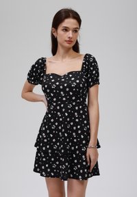 Czarna sukienka w kwiaty z kwadratowym dekoltem, puff sleeves, warstwowym fasonem i małymi różowymi i białymi wzorami stokrotek.
