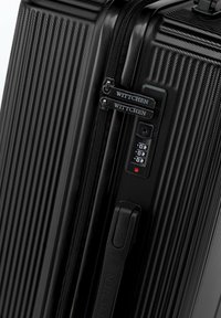 Black hard-shell suitcase with ribbed texture, dual zippers, and a combination lock. Features a sturdy handle and branded accents.