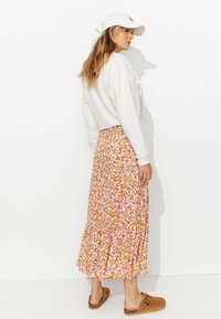 Jupe maxi florale avec des motifs roses, oranges et beiges ; ourlet volanté. Associée à un sweat-shirt blanc et des chaussures à enfiler marron.