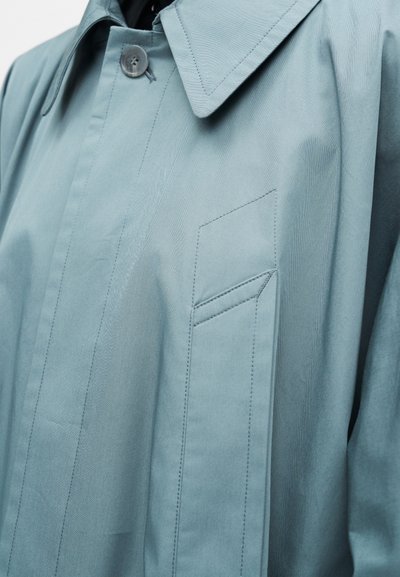 Világoskék ballonkabát hegyes gallérral, egysoros gombolással és finom varrási részletekkel díszített mellzsebbel.