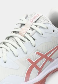 Λευκό αθλητικό παπούτσι με επάνω μέρος από δίχτυ, ροζ λεπτομέρειες και υφή με σχέδιο. Διαθέτει επίπεδα κορδόνια και εμφανές λογότυπο στη γλώσσα του παπουτσιού.