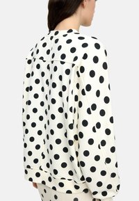 Biała bluza z dużymi czarnymi kropkami, z okrągłym dekoltem i ściągaczami przy rękawach. Gładka faktura i luźny krój.