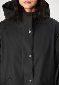 Svart vattentät jacka med huva, tryckknappsstängning och sidofickor med en slät, matt yta och rena designlinjer.