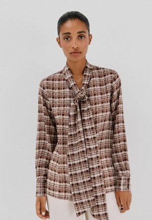 Bruin en crèmekleurig geruit shirt met een gestrikt kraagdetail, knoopmanchetten en een ontspannen pasvorm. Soepel materiaal met een subtiele glans.