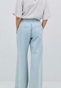 Helle blaue weit geschnittene Hose aus weichem Stoff, mit einem elastischen Bund und zwei Gesäßtaschen. Das Design ist schlicht und lässig.