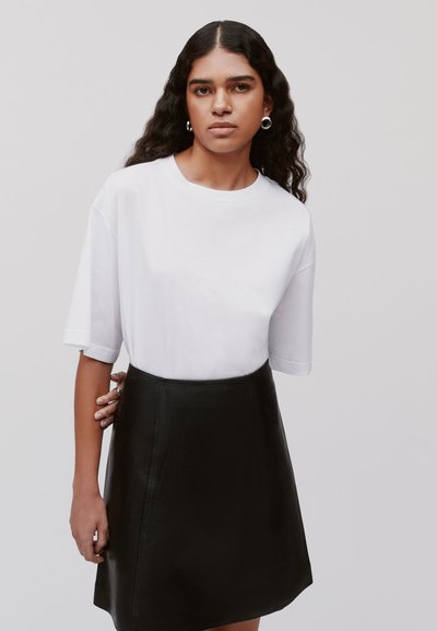 Witte T-shirt met korte mouwen en ronde hals, gecombineerd met een getailleerde zwarte leren minirok, die gladde texturen en schone lijnen laat zien.