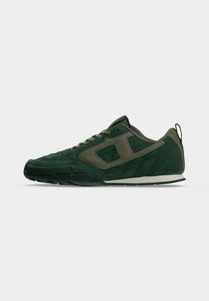 Chaussure de sport vert foncé avec des panneaux matelassés et en suède, un design à lacets et une semelle en caoutchouc noire sur un fond gris clair.