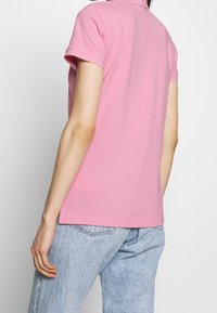 Polo rosa con un design aderente, maniche corte e un colletto discreto, abbinato a jeans di denim blu chiaro con una finitura testurizzata.