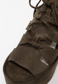 Chaussure plateforme en daim vert avec découpes et plusieurs options de laçage. Comprend une semelle épaisse pour un confort supplémentaire et une texture lisse.