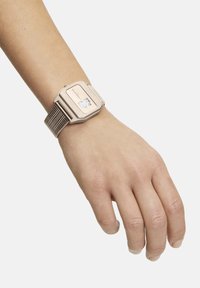 Orologio metallico dorato con quadrante rettangolare, bracciale in maglia e display trasparente. Nome del marchio visibile sul quadrante. Design elegante e moderno.