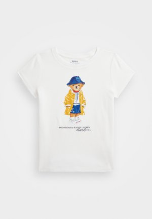 Chemise blanche à manches courtes avec un dessin d'ours portant un chapeau bleu, un imperméable jaune, un t-shirt rayé, un short bleu et des baskets blanches.