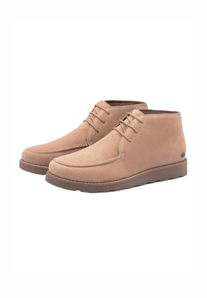 Botas de tobillo de ante beige con cordones a tono, detalles cosidos y suela de goma. Presentan una punta curva y un pequeño logo en el costado.