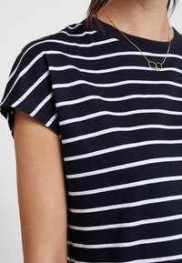 Marinblå bomulls-T-shirt med vita horisontella ränder, med korta ärmar och rund halsringning. Slät textur, avslappnad design.