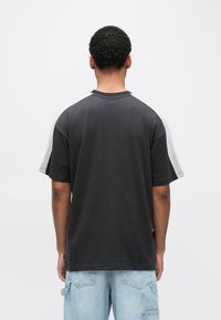 Μαύρο μπλουζάκι με γκρι λεπτομέρειες στα μανίκια, στρογγυλή λαιμόκοψη και άνετη εφαρμογή. Διαθέτει ταμπελάκι στο κάτω αριστερό μέρος. Υλικό από βαμβάκι.